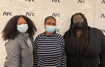 Three Arc/Morris staff wearing masks stand in front of a white banner with the Arc/Morris logo at the Years of Service event.