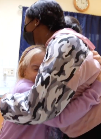 A caregiver wearing a mask hugs her female resident.