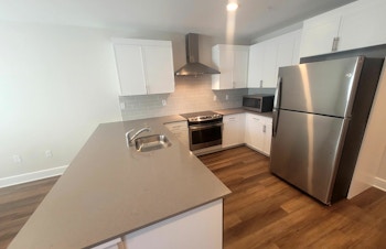The kitchen at Florham Park Supported Apartments featuring hardwood floors, white cabinets and stainless steel appliances.