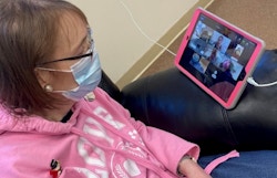 A woman sits in a chair watching a video on a tablet device.