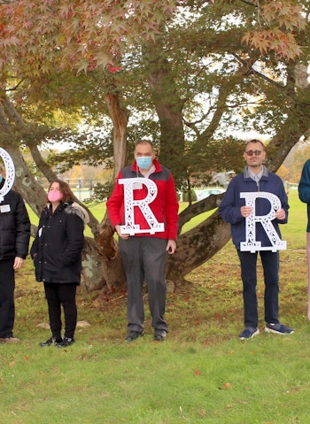 Seven individuals we serve stand in front of a tree holding large letters which spell out Morris.