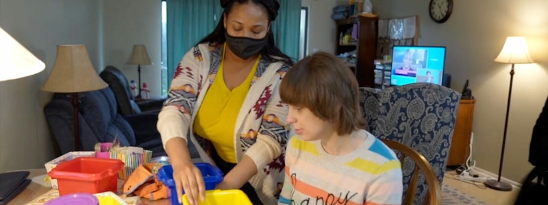 An Arc Morris staff member wears a mask while assisting a resident with an in-home activity using multi-colored buckets.