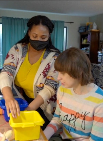 An Arc Morris staff member wears a mask while assisting a resident with an in-home activity using multi-colored buckets.