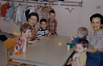 A vintage photo of two adult women seated at a table with five children.
